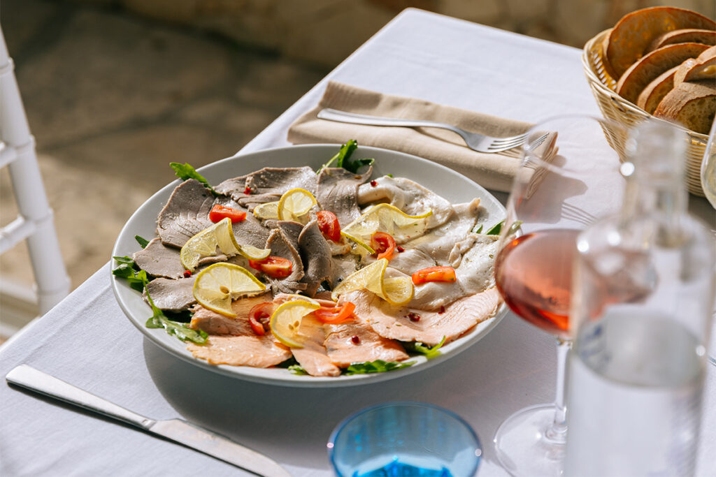 Crudo di pesce con rucola, limone e pomodorini, con il cestino del pane e il rosato accanto