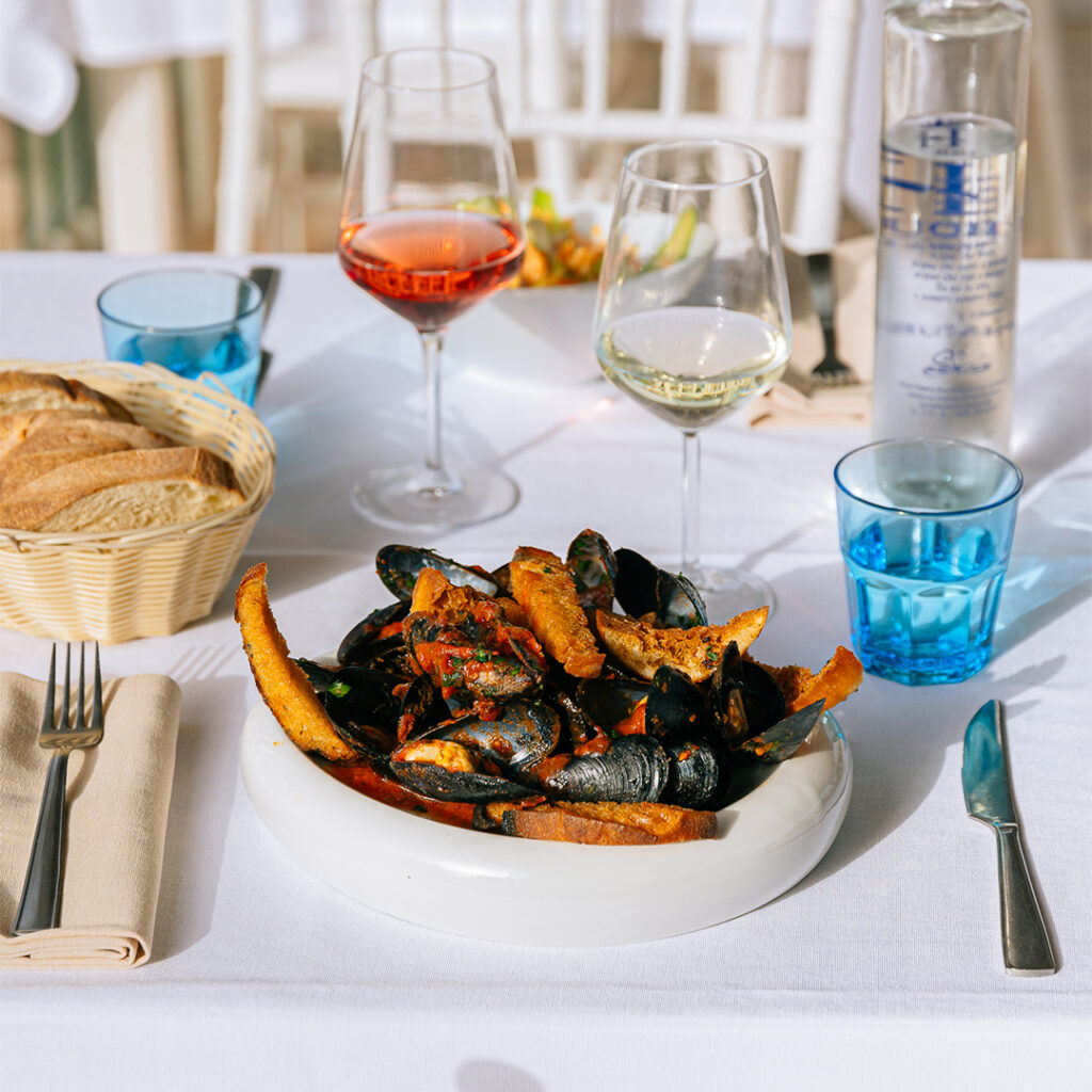 Cozze in salsa con crostoni al centro del tavolo, con il pane, il vino bianco e il rosato