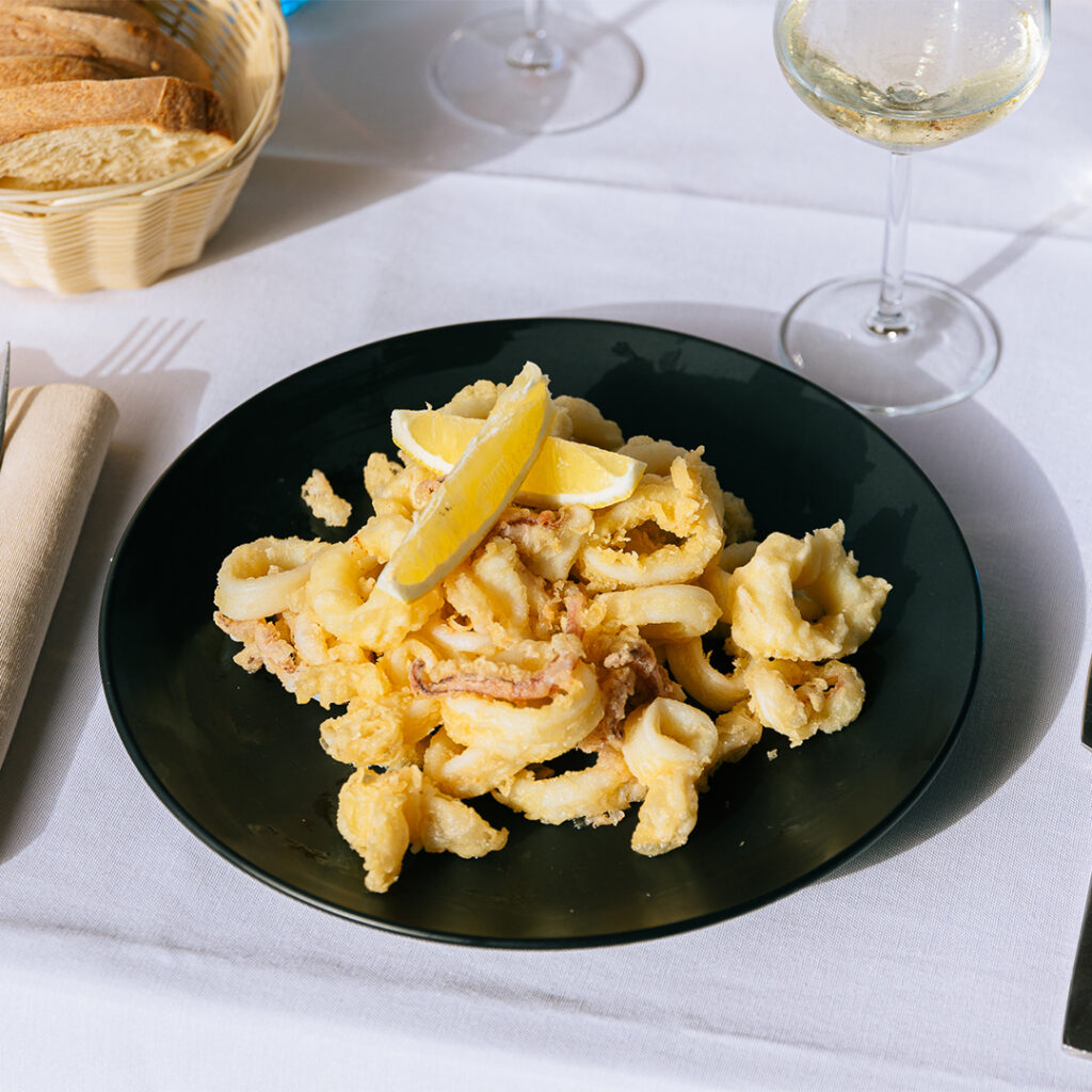 Frittura di calamari dorati con spicchio di limone su piatto nero