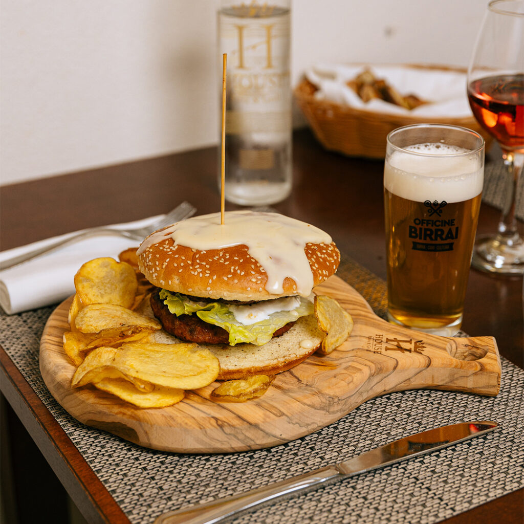 House Burger con cipolla caramellata e chips di patate, servito sul tagliere di legno inciso col marchio House